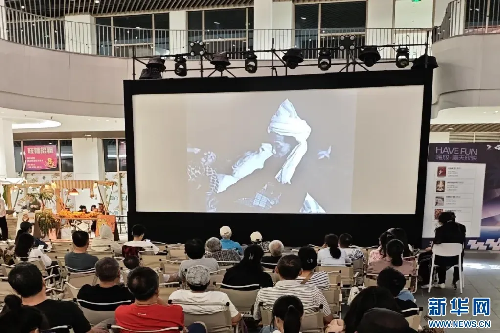 第七届三亚夏日站中央广场露天放映实拍，观众面向大银幕，后方为商场中庭